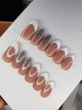 Black and nude stiletto press-on nails with rhinestone clusters in a clear case
